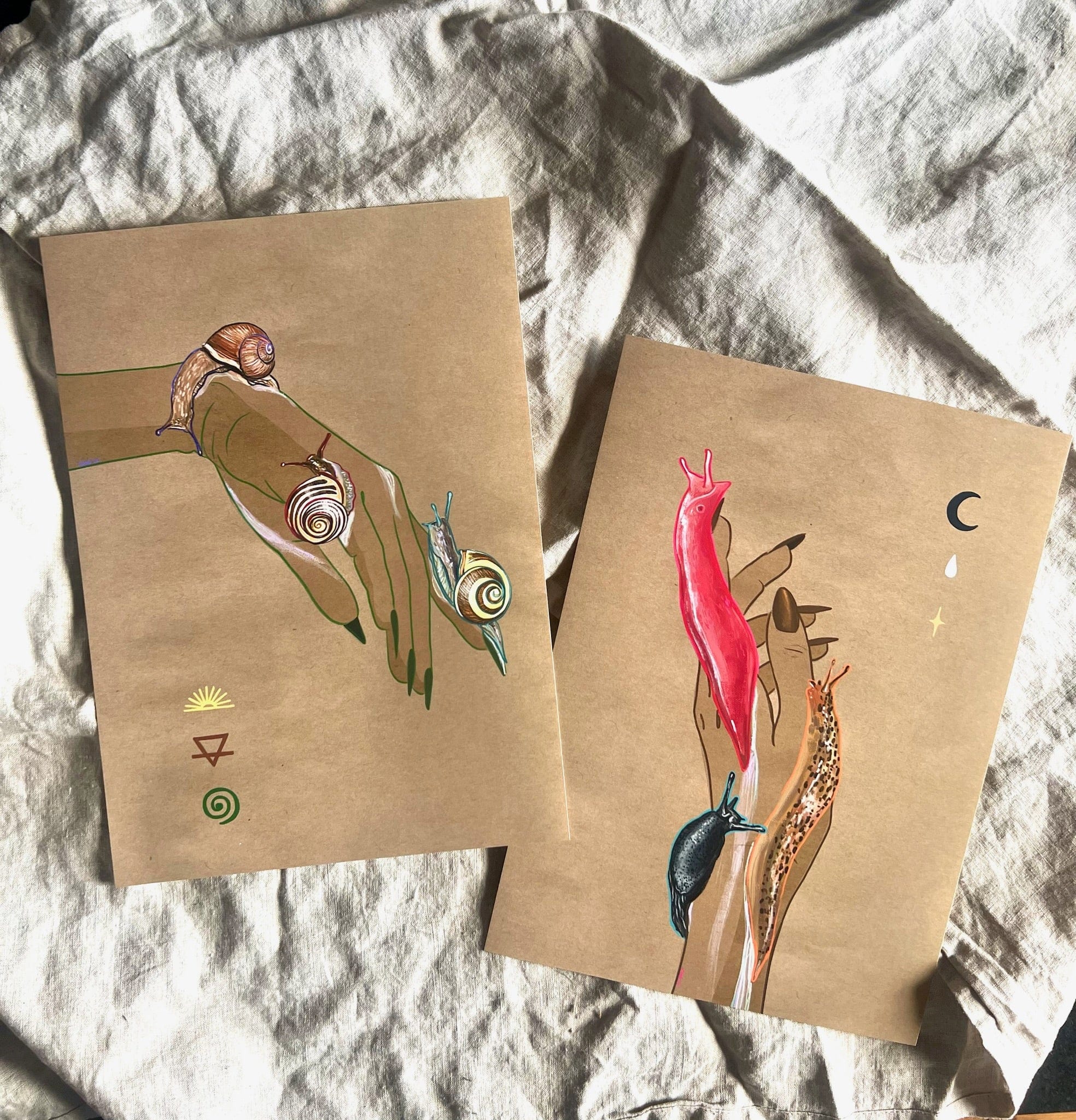 The Spring Snails Matte Art Print by Beauty and the Beastie captures nature's charm with spiral-shelled snails on a hand and vibrant slugs. Nearby symbols, including a crescent moon and sun, add mystique to the brown paper illustrations.