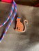 A charming ginger Léopard Roux Pin by Pins by diedododa features a freckled face and "Leopard Roux has Bonnet" on its body, attached with a stylish red and blue striped rope.