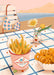 Frites Vites Giclée Art Print by Hôtel Dodo captures a carefree summer vibe with French fries, curly fries, a flower vase, bench, and bikini top on a seaside picnic table.
