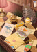 A tabby cat sits on a checkered desk surrounded by stationery, a quirky keychain, a yellow envelope, a candy bar, a cupcake, helpful travel guides titled “Road Tripping Guide” and “Edinburgh Trip,” and the Highland Tiger Lodge Giclée Art Print from Hôtel Dodo.
